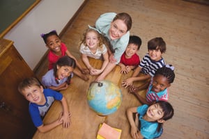 Young students smiling around a globe in classroom with a teacher